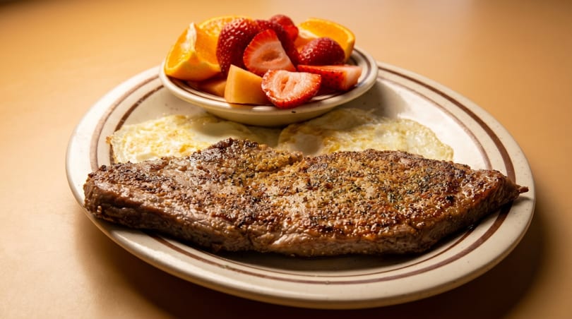 Steak and eggs breakfast with a side of fresh fruit including strawberries and oranges.