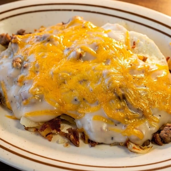 Hearty breakfast skillet with sausage, potatoes, gravy, and melted cheddar cheese on a white plate.