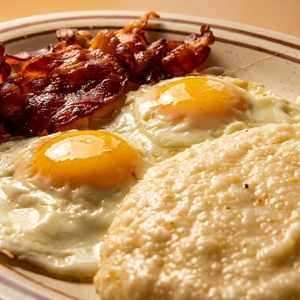 A breakfast plate with two fried eggs, crispy bacon, and a serving of creamy grits.