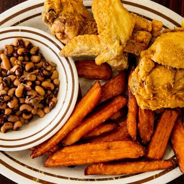 Fried chicken, sweet potato fries, and a bowl of black-eyed peas on a white plate.